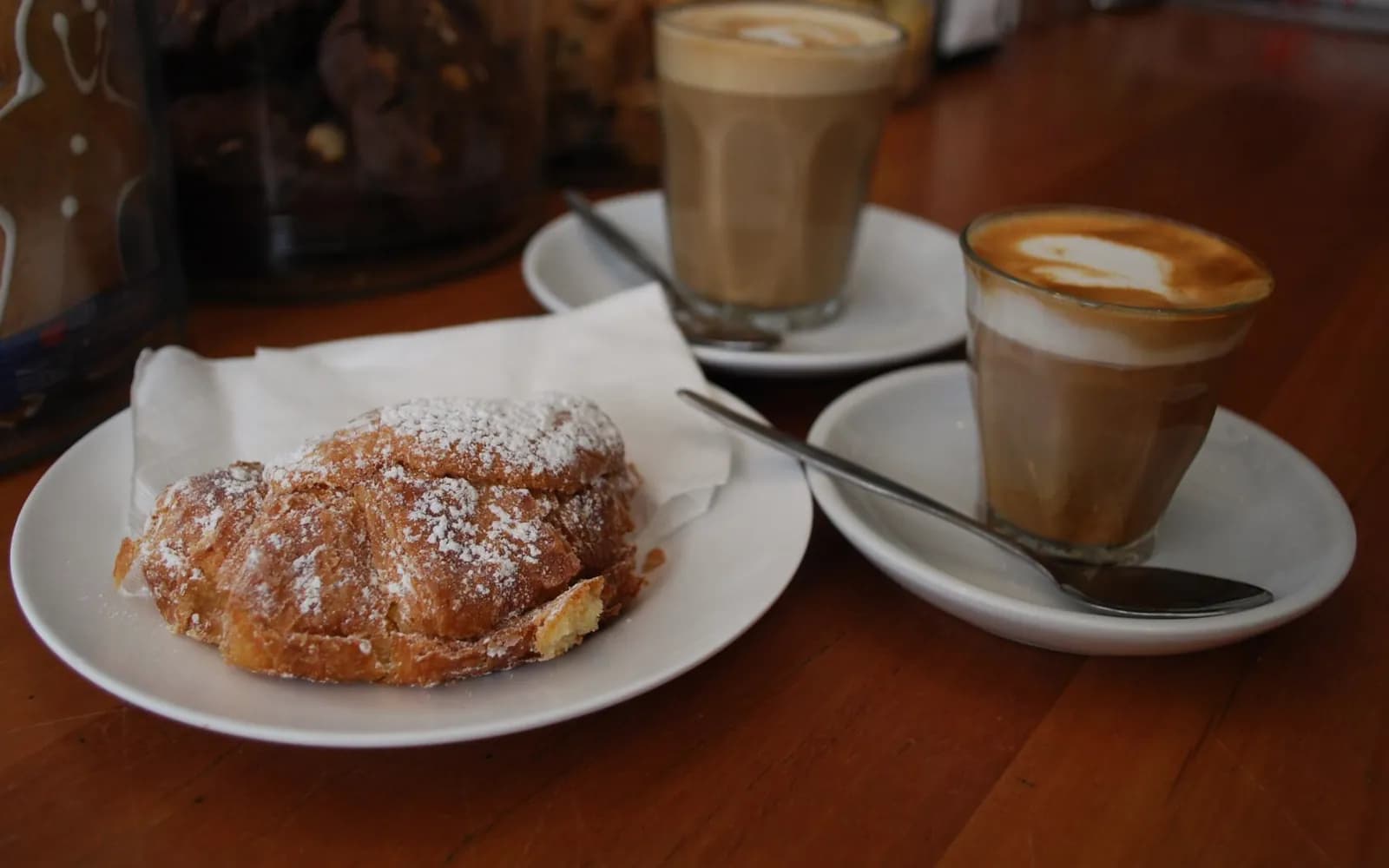 Un croissant cu migdale și două cafele cu lapte pe o masă