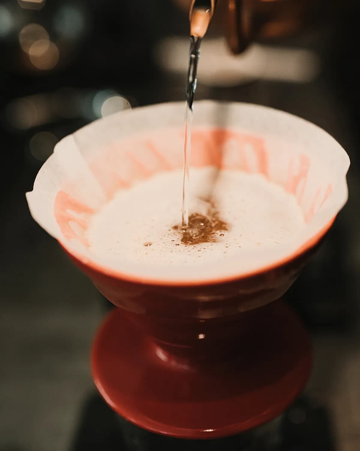 Un dripper V60 roșu cu filtru de hârtie, sub un fir subțire de apă